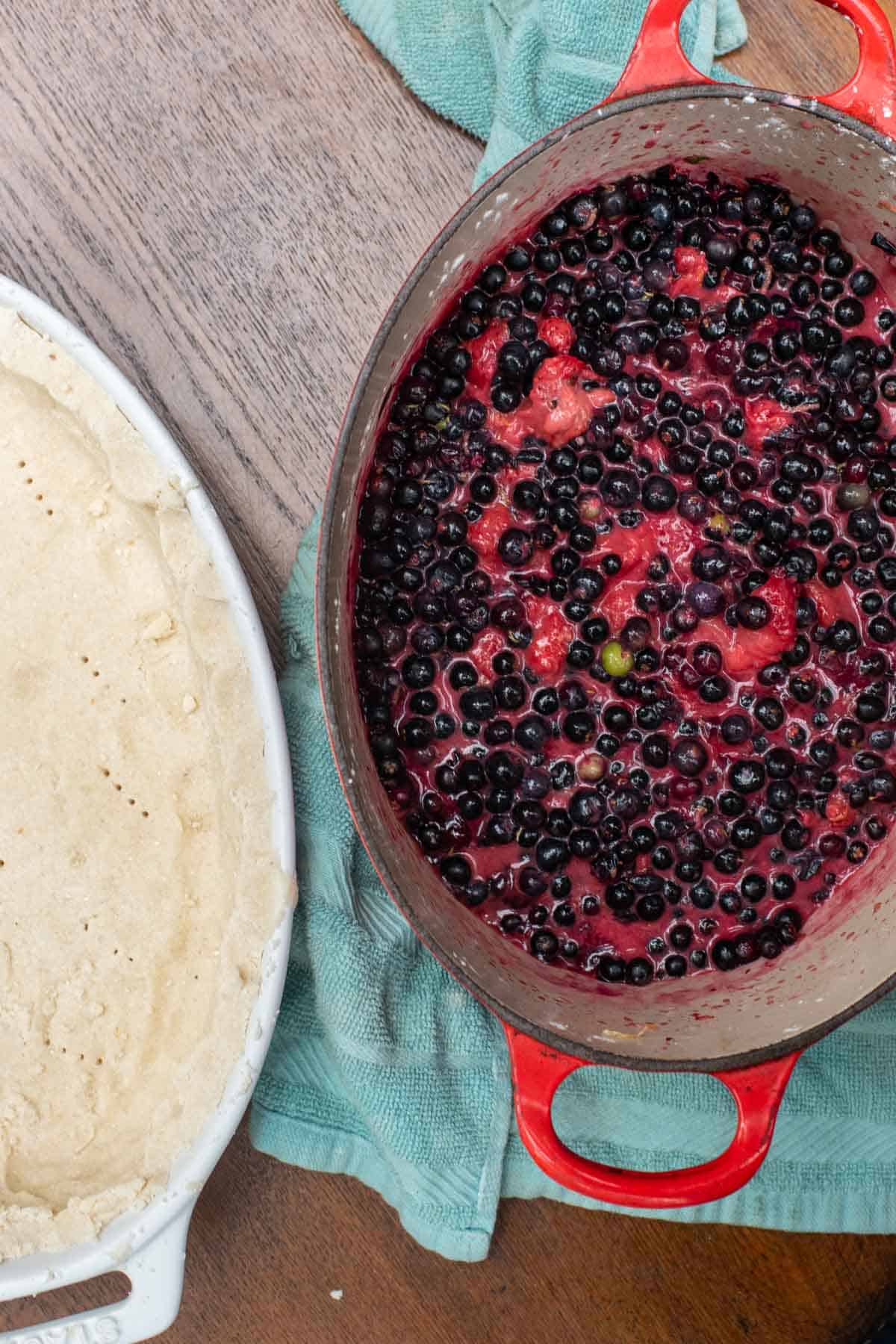 stovetop cooked blueberries in pot and AIP pie crust in baking dish